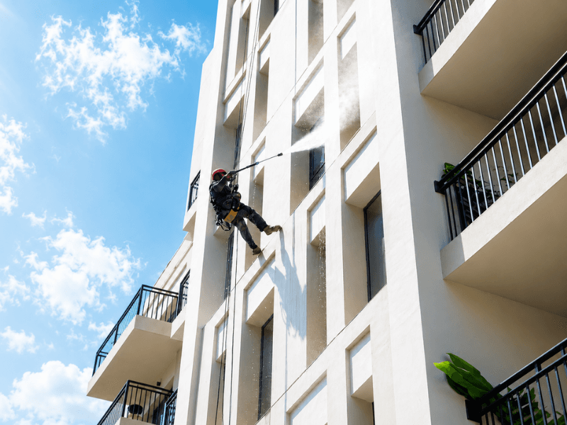 A rope access technician pressure washing the external white facade of Hayat Boulevard Apartments